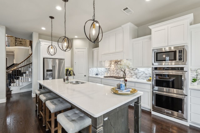 kitchen featuring pendant lighting, sink, appliances with stainless steel finishes, white cabinetry, and an island with sink