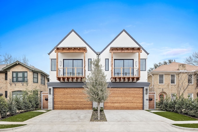 view of front facade with a balcony, an attached garage, concrete driveway, and stucco siding