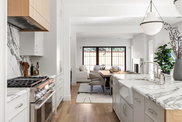 kitchen with light wood-style floors, open floor plan, a sink, high end range, and wall chimney exhaust hood