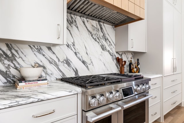 kitchen with custom range hood, white cabinets, backsplash, and high end stainless steel range