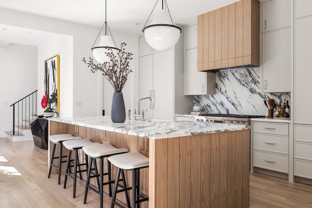 kitchen featuring light wood-type flooring, a breakfast bar area, decorative backsplash, and light stone countertops