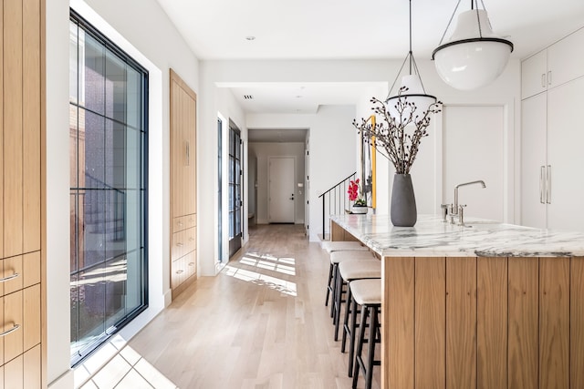 kitchen with light wood-type flooring, modern cabinets, a breakfast bar area, and light stone counters