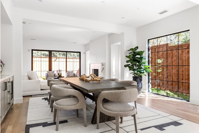 dining space with a healthy amount of sunlight, light wood-type flooring, a premium fireplace, and visible vents