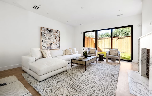 living room featuring light wood-style floors, visible vents, a fireplace, and baseboards