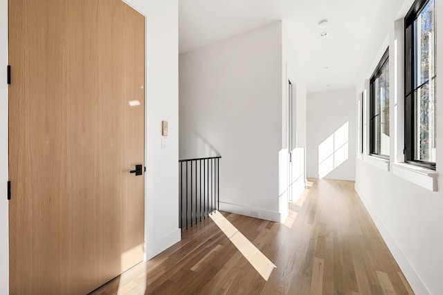 hall featuring an upstairs landing, baseboards, and wood finished floors