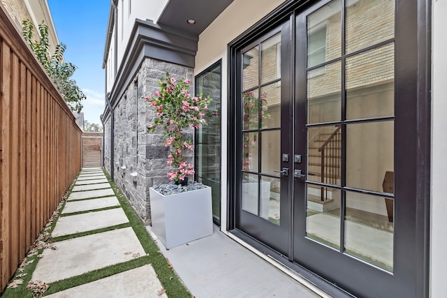 view of exterior entry featuring stone siding, fence, and french doors