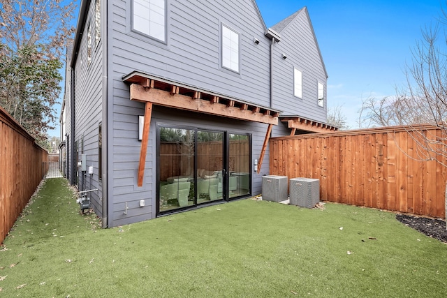 rear view of property with cooling unit, a fenced backyard, and a lawn