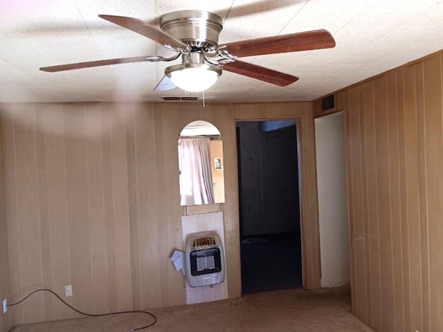 carpeted empty room featuring ceiling fan, heating unit, and wood walls