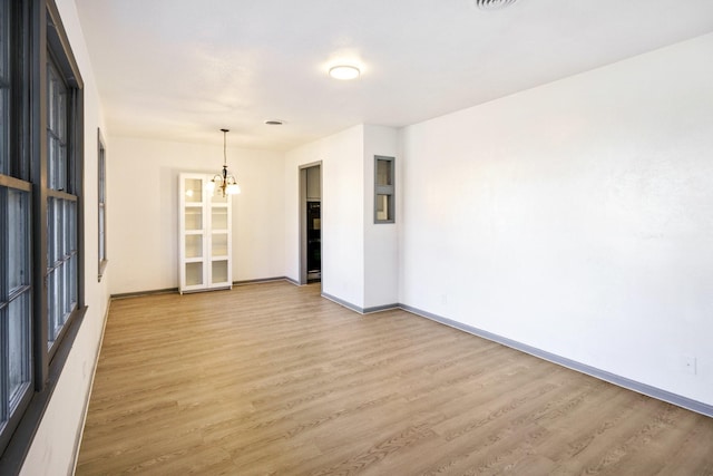 unfurnished room with a chandelier and light hardwood / wood-style floors