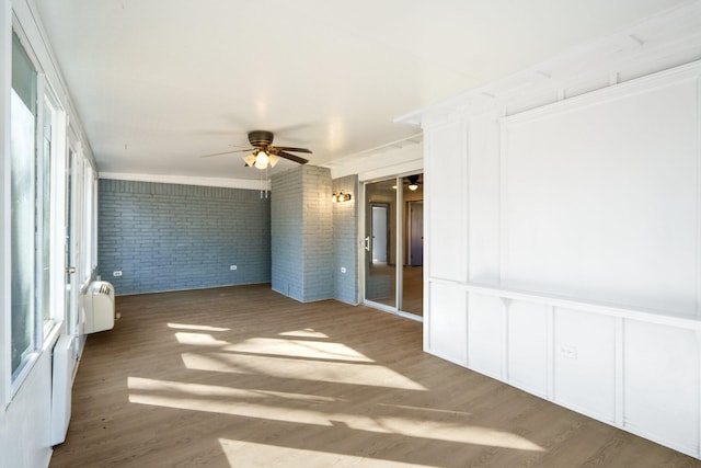 unfurnished room with wood-type flooring, brick wall, radiator, and plenty of natural light