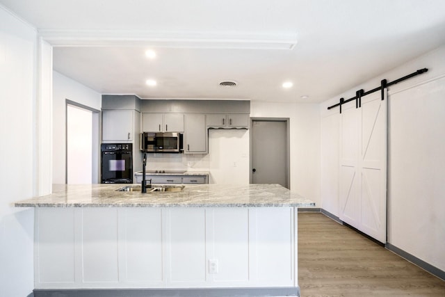 kitchen featuring gray cabinetry, light stone counters, black appliances, kitchen peninsula, and a barn door