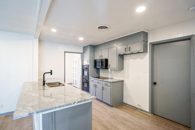 kitchen with sink, gray cabinetry, light hardwood / wood-style floors, black appliances, and light stone countertops