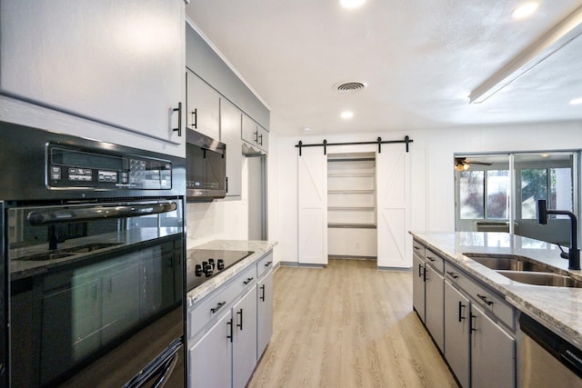 kitchen featuring sink, black appliances, light stone countertops, a barn door, and light wood-type flooring