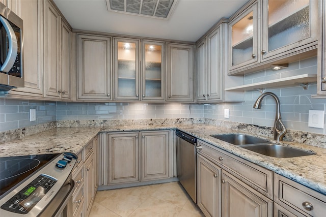 kitchen with stainless steel appliances, sink, backsplash, and light stone counters