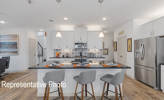 kitchen with pendant lighting, white cabinetry, appliances with stainless steel finishes, and a center island with sink