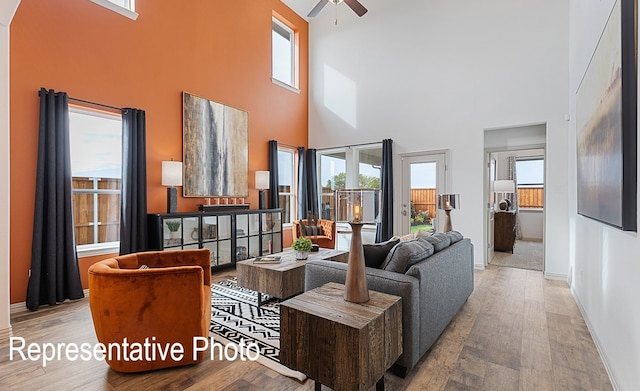 living room with a high ceiling, ceiling fan, a wealth of natural light, and light hardwood / wood-style floors