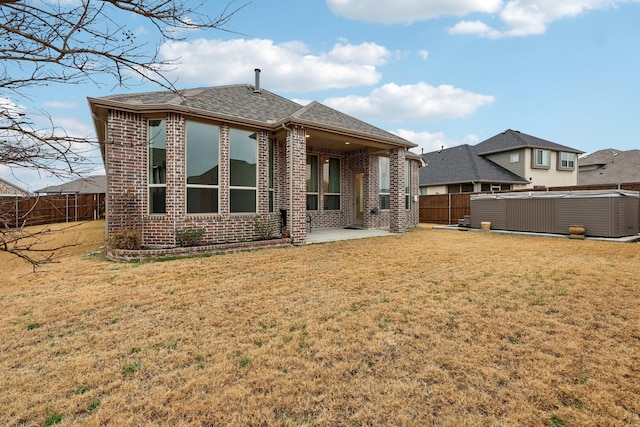 rear view of property featuring a hot tub, a patio, and a lawn