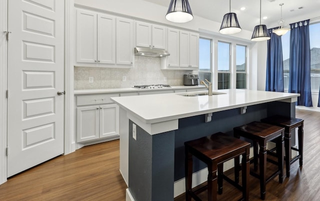 kitchen featuring pendant lighting, hardwood / wood-style flooring, a breakfast bar area, an island with sink, and white cabinets