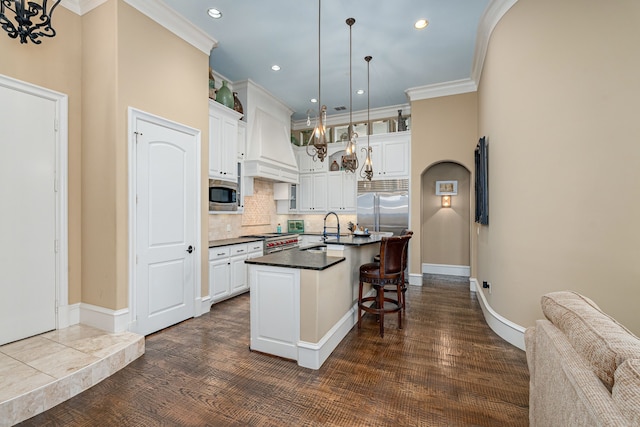 kitchen featuring dark countertops, built in appliances, crown molding, premium range hood, and a sink