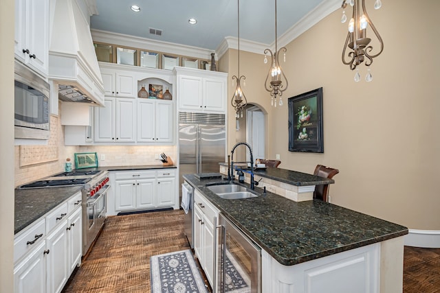 kitchen with beverage cooler, arched walkways, built in appliances, custom exhaust hood, and a sink