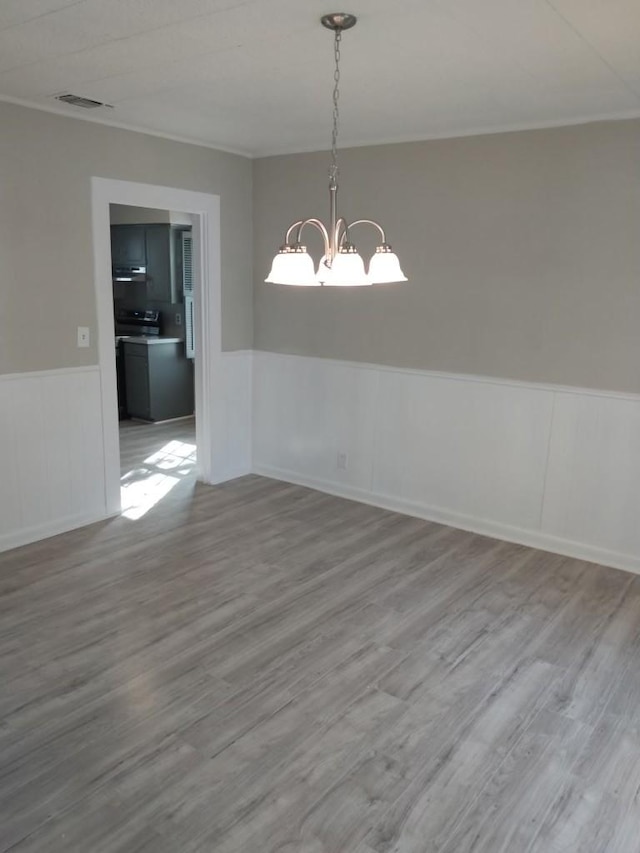 unfurnished dining area featuring hardwood / wood-style flooring, ornamental molding, and a notable chandelier