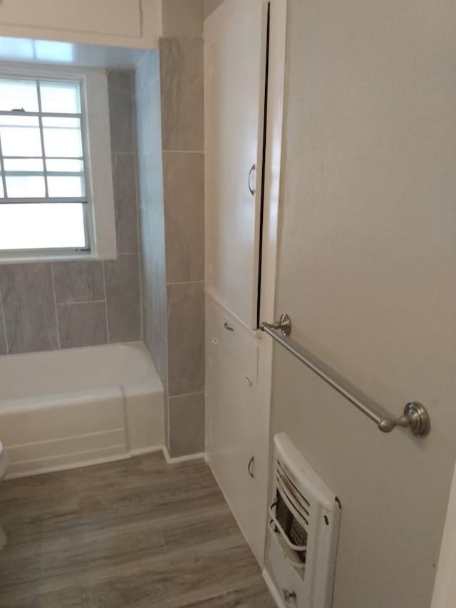 bathroom with hardwood / wood-style flooring, tiled shower / bath, toilet, and heating unit