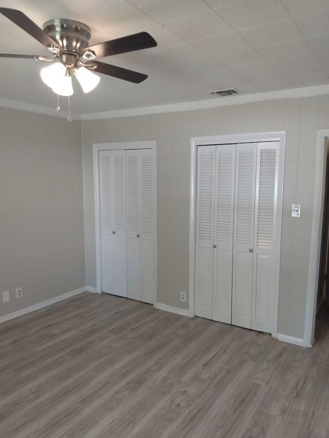 unfurnished bedroom with multiple closets, wood-type flooring, ceiling fan, and crown molding