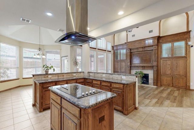 kitchen with a kitchen island, dark stone countertops, hanging light fixtures, island exhaust hood, and black electric stovetop