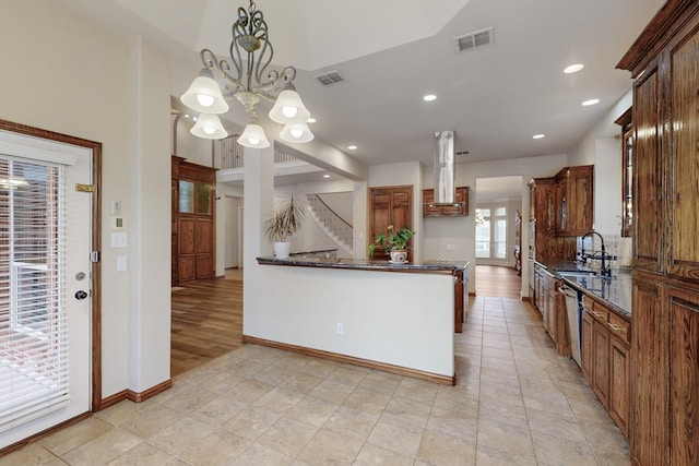 kitchen featuring sink, dark stone countertops, hanging light fixtures, stainless steel dishwasher, and kitchen peninsula