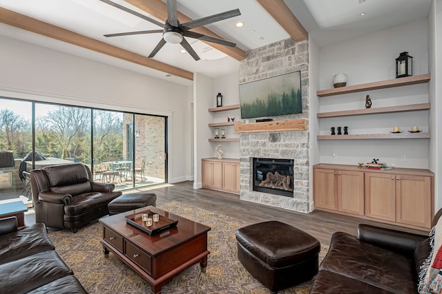 living room featuring beam ceiling, dark wood-type flooring, a stone fireplace, and ceiling fan