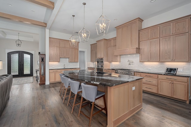 kitchen featuring a breakfast bar, decorative light fixtures, dark stone countertops, a center island with sink, and french doors