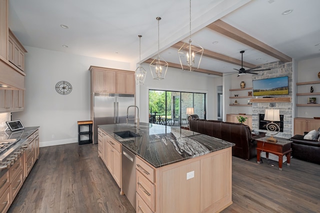 kitchen with sink, light brown cabinets, hanging light fixtures, and a center island with sink