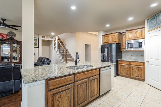 kitchen featuring sink, appliances with stainless steel finishes, tasteful backsplash, light stone countertops, and an island with sink