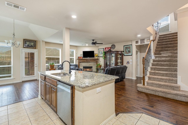 kitchen with light tile patterned flooring, sink, stainless steel dishwasher, light stone countertops, and a center island with sink