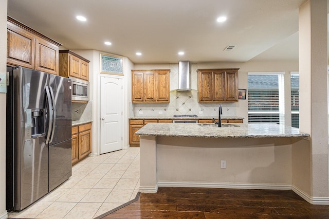 kitchen featuring sink, wall chimney range hood, stainless steel appliances, light stone countertops, and backsplash