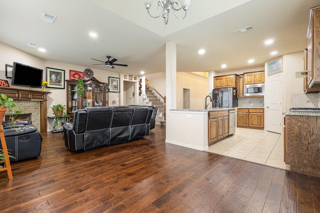 kitchen with tasteful backsplash, a brick fireplace, a center island with sink, light wood-type flooring, and appliances with stainless steel finishes