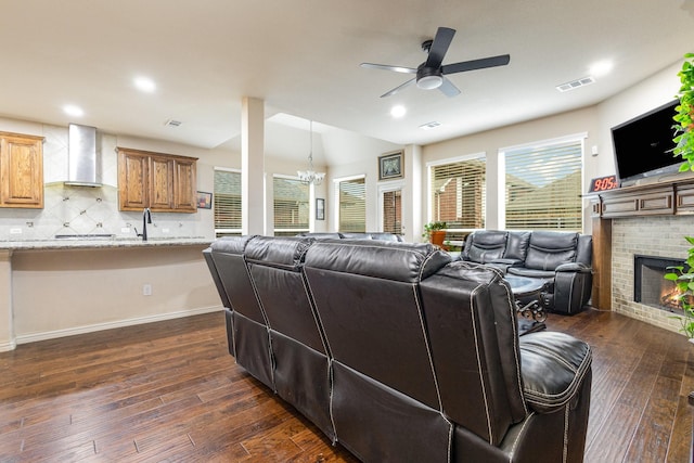 living room with dark wood-type flooring, sink, vaulted ceiling, a fireplace, and ceiling fan with notable chandelier