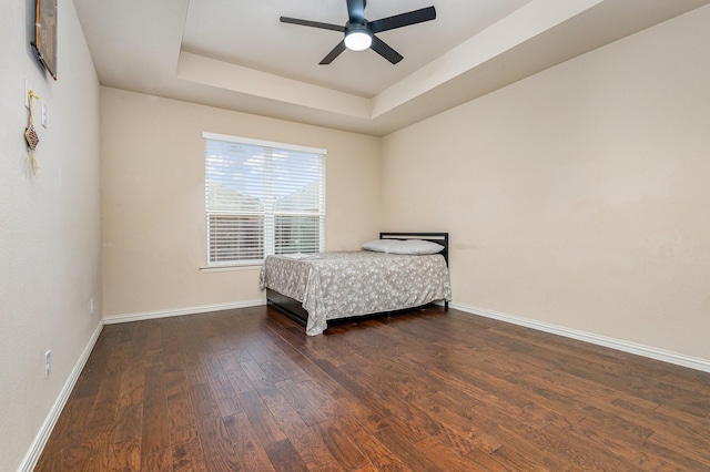 bedroom with ceiling fan, dark hardwood / wood-style floors, and a raised ceiling