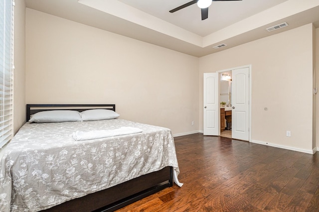 bedroom featuring dark wood-type flooring, a raised ceiling, ceiling fan, and ensuite bathroom