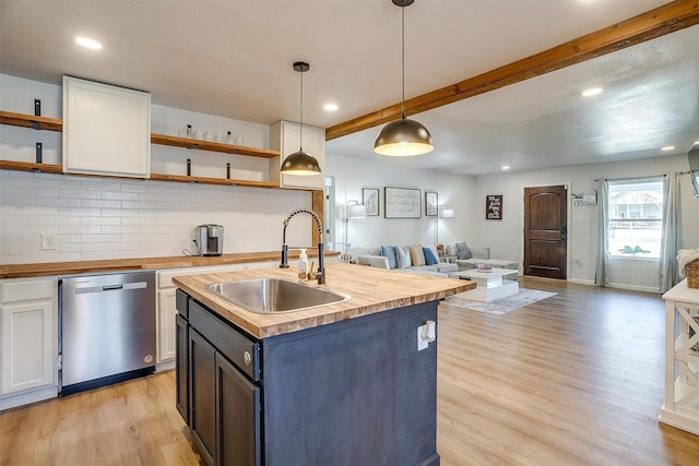 kitchen with butcher block counters, sink, hanging light fixtures, stainless steel dishwasher, and white cabinets