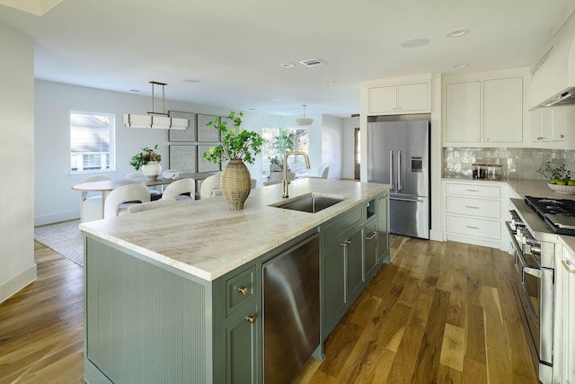 kitchen featuring pendant lighting, appliances with stainless steel finishes, white cabinetry, custom range hood, and an island with sink