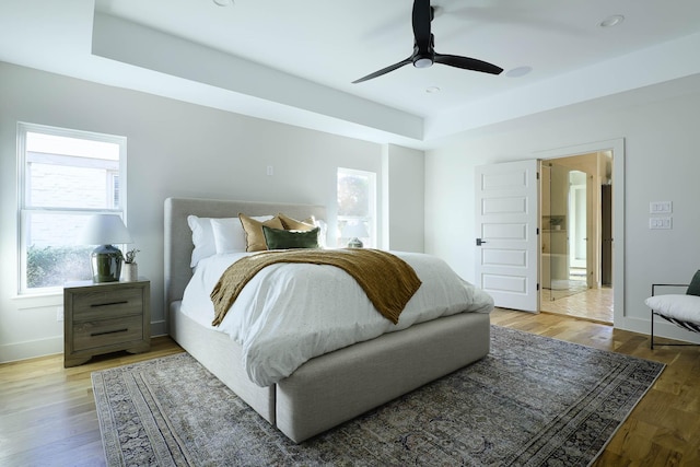 bedroom with a raised ceiling, wood-type flooring, and ceiling fan