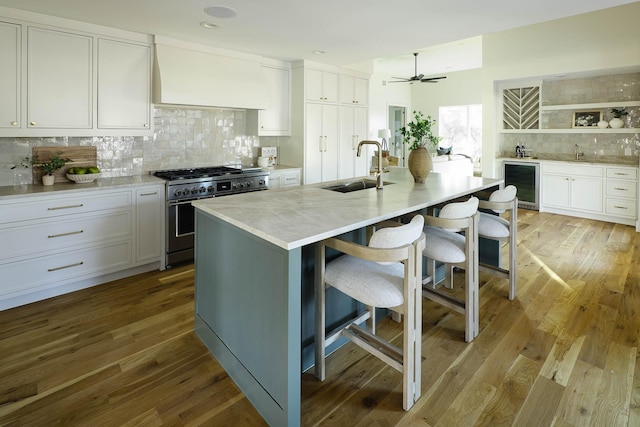 kitchen with high end stove, an island with sink, sink, a kitchen bar, and custom range hood