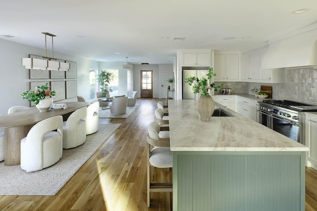 kitchen with hanging light fixtures, appliances with stainless steel finishes, an island with sink, hardwood / wood-style floors, and white cabinets