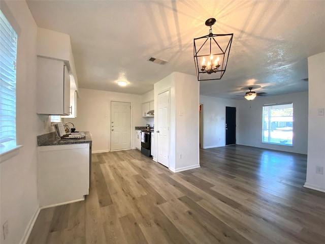 kitchen with stainless steel electric stove, hardwood / wood-style floors, decorative light fixtures, white cabinetry, and sink