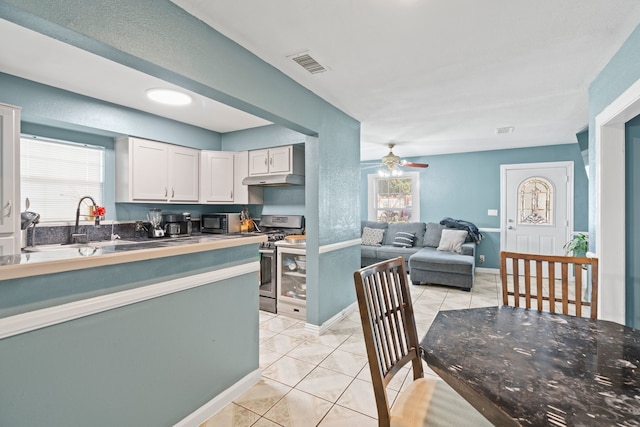 kitchen with light tile patterned floors, sink, stainless steel gas range, ceiling fan, and white cabinets