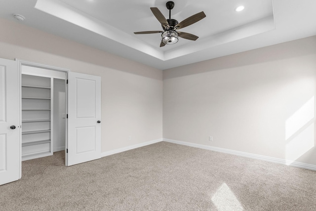 unfurnished bedroom with a walk in closet, carpet, ceiling fan, a raised ceiling, and a closet