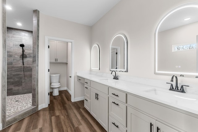 bathroom featuring hardwood / wood-style flooring, vanity, tiled shower, and toilet