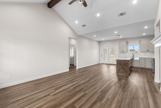 unfurnished living room featuring high vaulted ceiling, beamed ceiling, sink, ceiling fan, and dark wood-type flooring