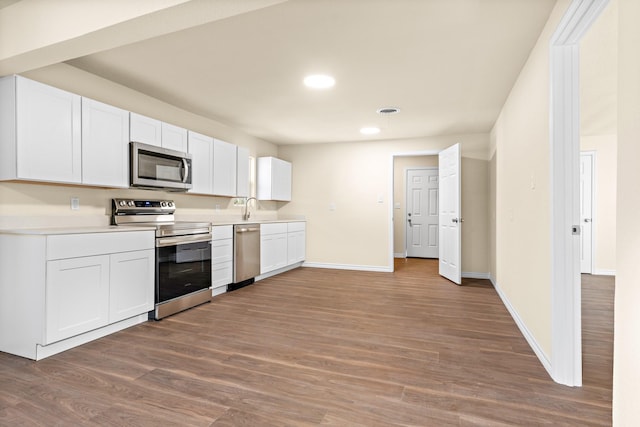 kitchen with stainless steel appliances, sink, hardwood / wood-style floors, and white cabinets